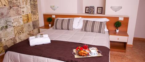 A neatly made bed with a brown blanket, a tray of breakfast including croissants, fruit, and a cup of coffee, and a stone wall with a map design.