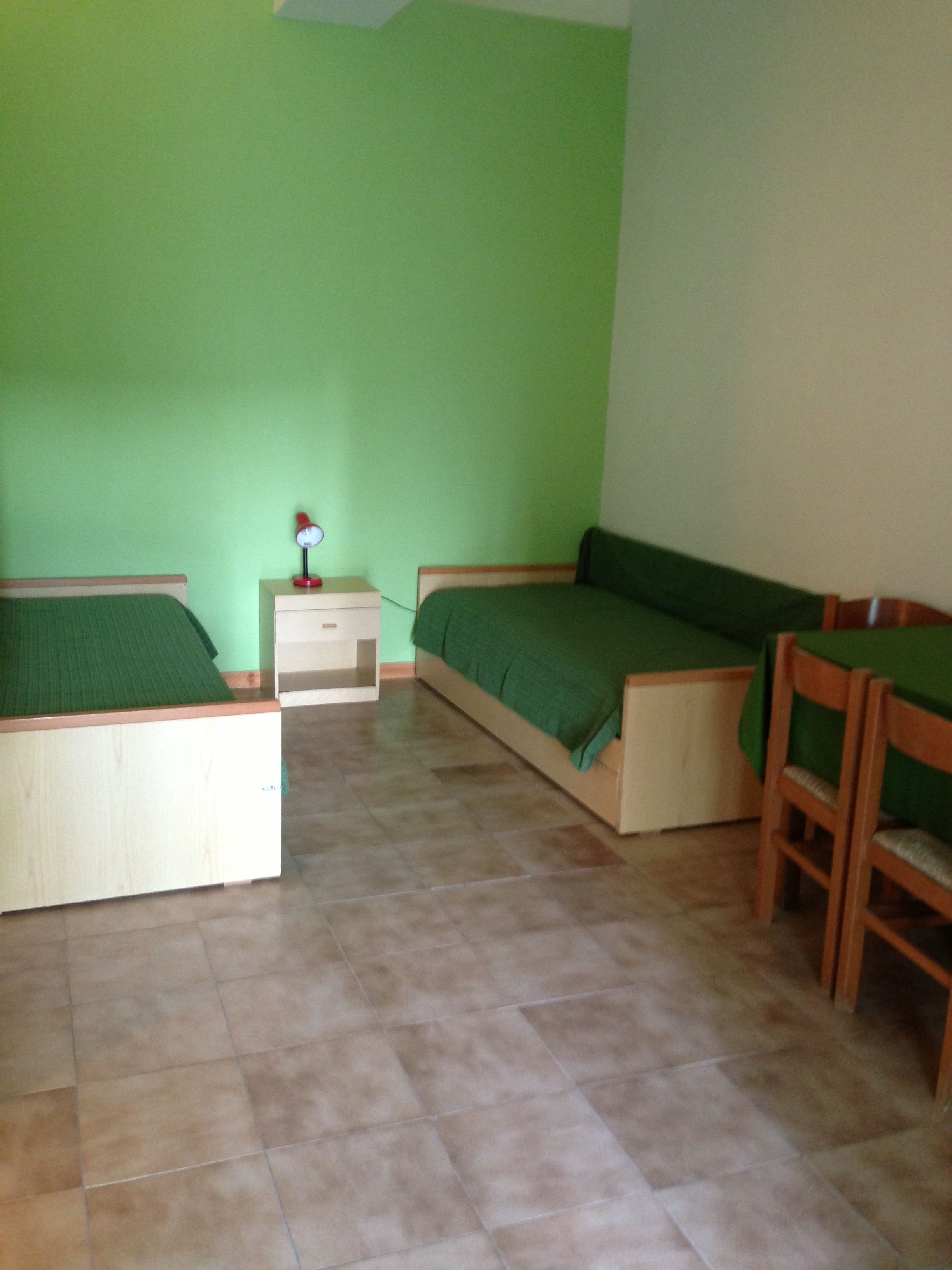 Una habitación con dos camas individuales, una mesita de noche, un escritorio y una silla.