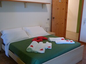 Un lit bien fait, avec du linge de lit blanc et une couette verte, une porte en bois et une petite table de chevet avec une lampe.