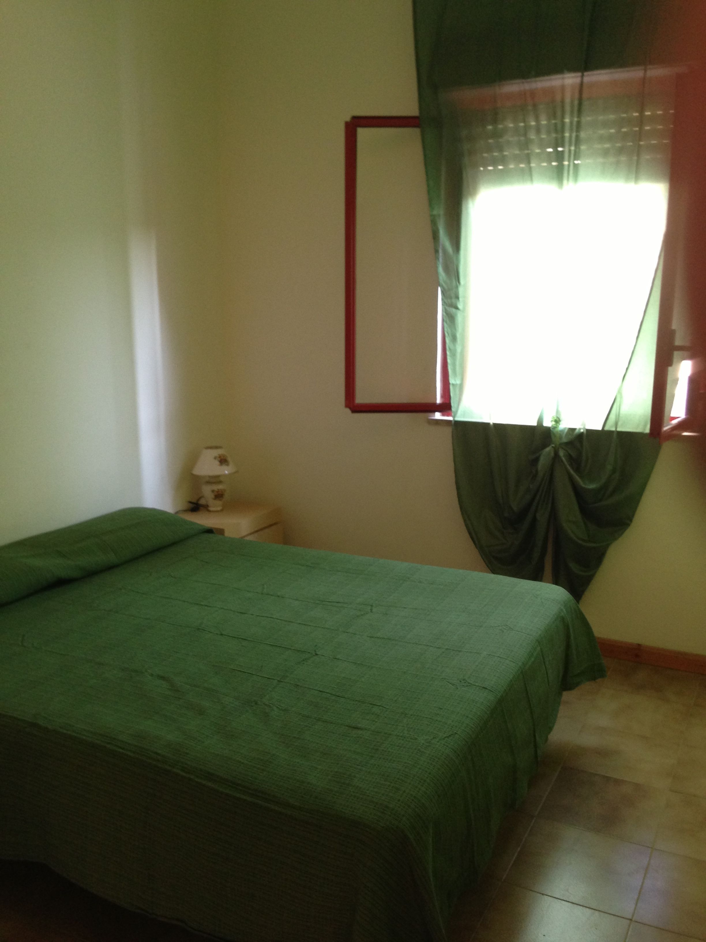 A bedroom with a bed, a nightstand, a lamp, and a window with curtains.