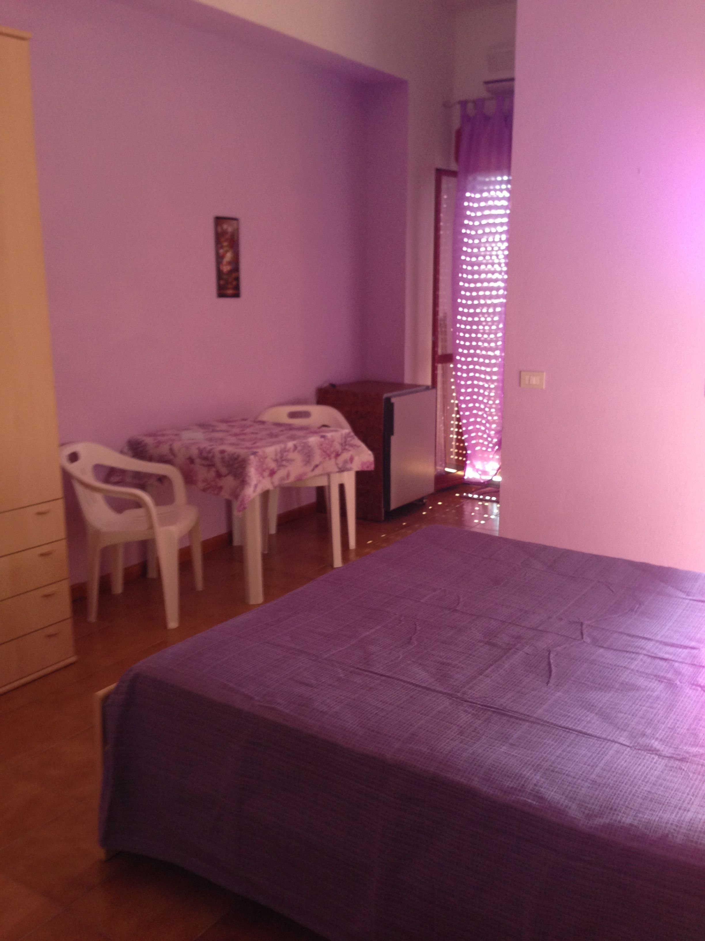 A room with a bed, a small table, two chairs, a dresser, and a window with curtains.