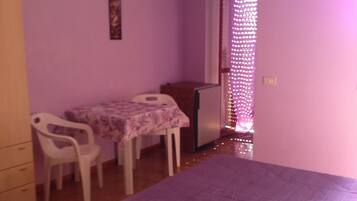 A room with a bed, a small table, two chairs, a dresser, and a window with curtains.