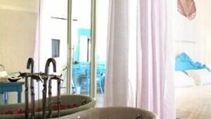 A bathroom with a bathtub filled with water and rose petals, a sink, and a mirror. - The Heritage Baan Silom Hotel (Bangkok)