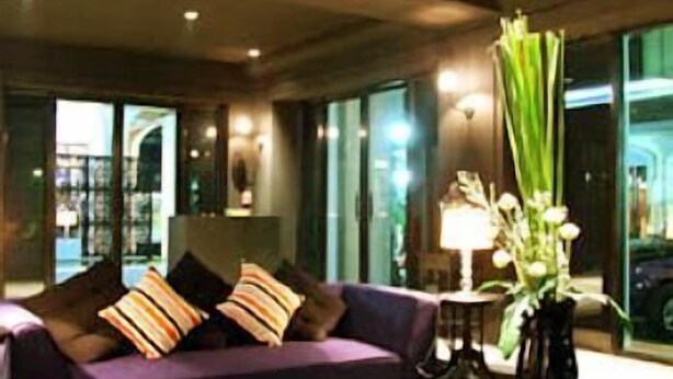 A modern hotel lobby with a purple sofa, a vase of flowers, and large windows. - The Heritage Baan Silom Hotel (Bangkok)