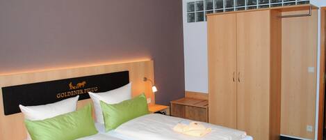 Une chambre d’hôtel avec deux lits, une tête de lit ornée d’un logo, une armoire et une table de chevet avec une lampe.