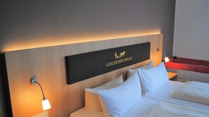 A hotel room with a bed, white pillows, a nightstand with a lamp, and a sign on the headboard reading "GOLDENER PFUG". - Landgasthof Goldener Pflug (Frasdorf)
