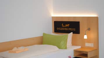 A hotel room with a bed, a nightstand, a wall-mounted sign, and a bedside table with a lamp.
