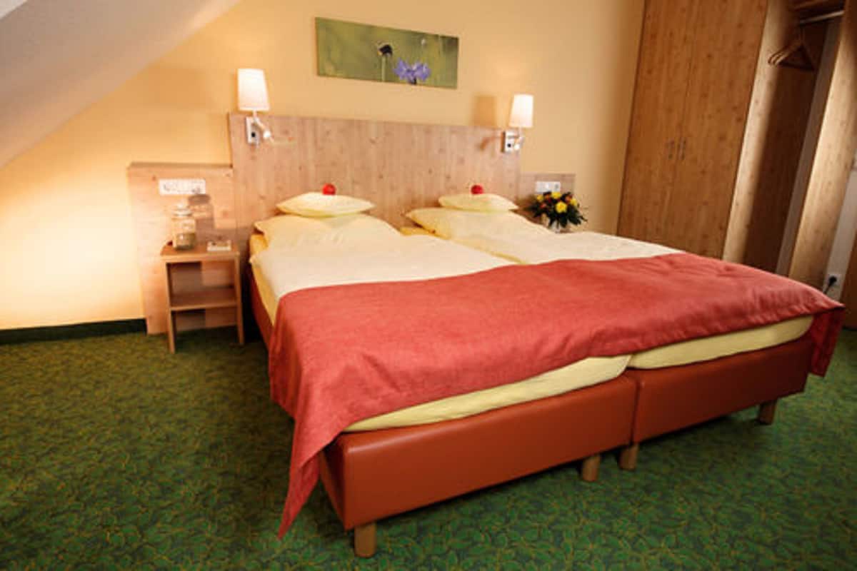 A hotel room with a double bed, two bedside tables, a nightstand, a wooden headboard, and a green carpet.