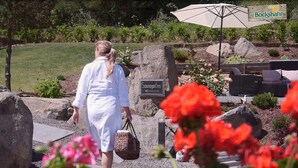 A woman in a white dress walking towards a sign that reads "Sundagarten" in a garden area with a wicker basket, red flowers, and outdoor furniture. - Hotel und Landgasthof Zum Bockshahn (Spessart)