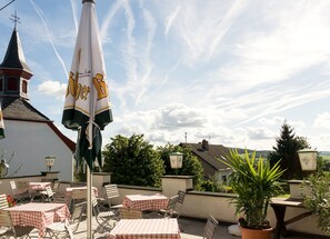 An outdoor seating area with tables and chairs, a large umbrella, and a view of buildings and trees in the background. - Hotel und Landgasthof Zum Bockshahn (Spessart)