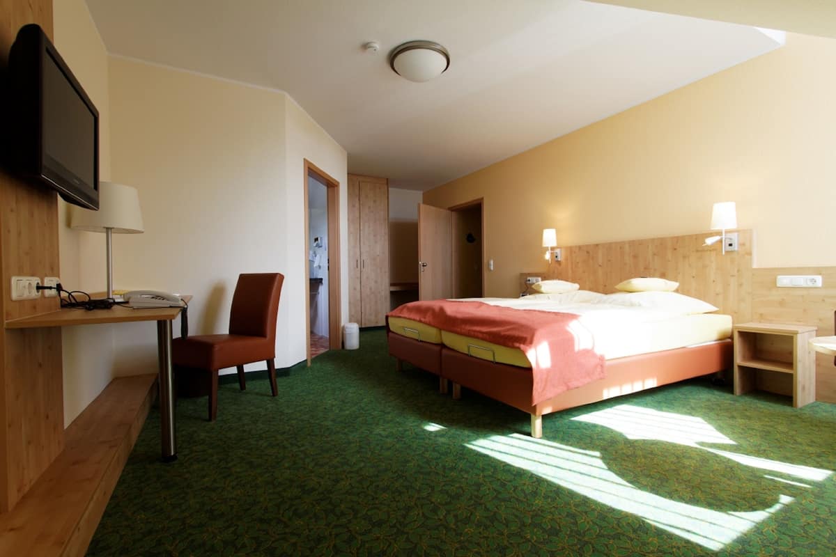 A hotel room with a bed, a desk with a telephone, a chair, and a television mounted on the wall.