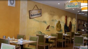 A restaurant with wooden tables and green chairs, a mural on the wall, and a sign that reads "Hahnenkorb". - Hotel und Landgasthof Zum Bockshahn (Spessart)