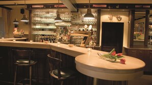 A bar area with multiple stools, a counter with a vase of flowers, and shelves stocked with bottles and glasses. - Hotel und Landgasthof Zum Bockshahn (Spessart)
