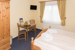 A room with a wooden bed, a desk with a chair, a television mounted on the wall, and a window with curtains. - Hotel und Landgasthof Zum Bockshahn (Spessart)