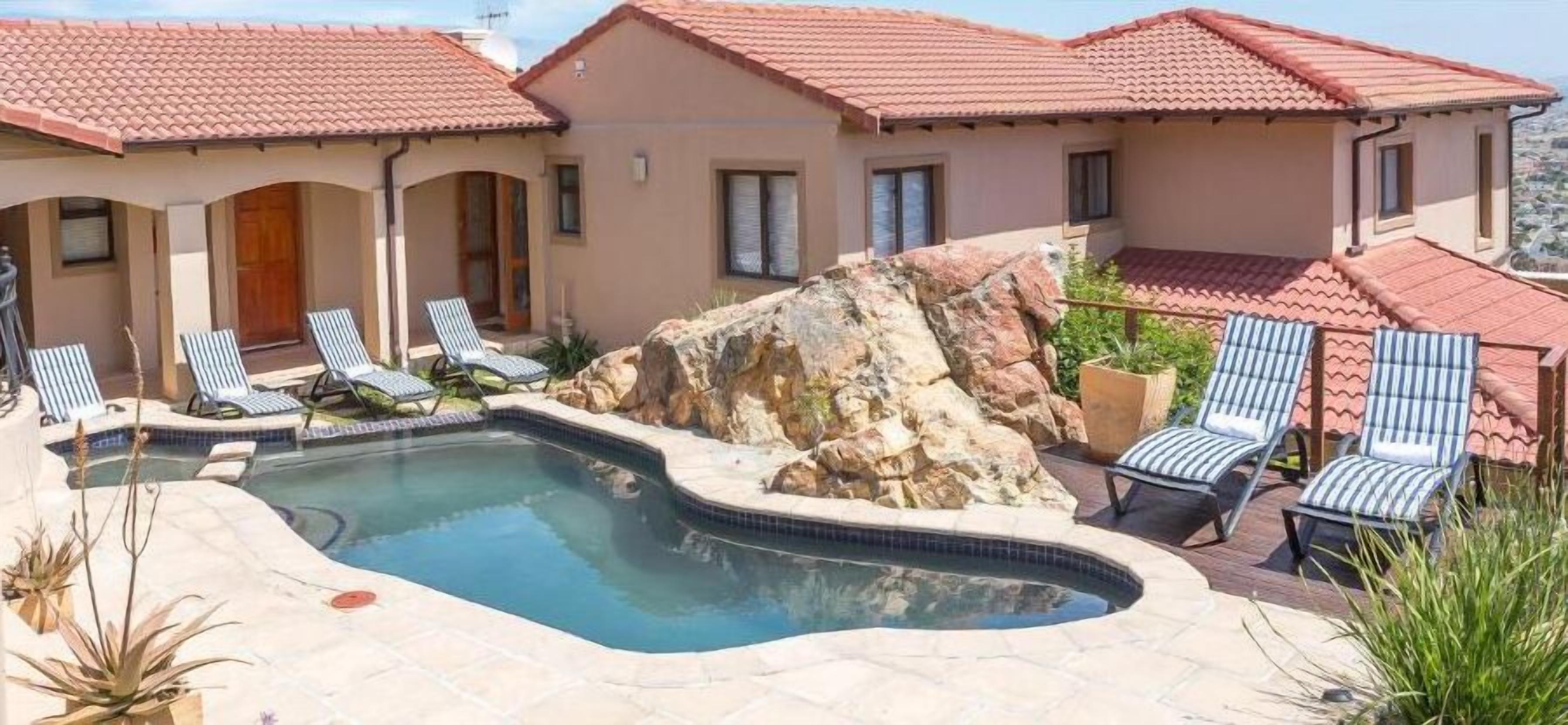 A pool area with lounge chairs, a hot tub, and a rock formation.