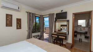 A hotel room with a bed, a desk, a chair, a television, a bathroom with a sink and mirror, and a balcony with curtains. - Blue Horizon Guest House (Cape Town)