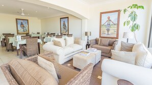 A spacious living area with a white sofa, wicker chairs, and a dining area with tables and chairs. - Blue Horizon Guest House (Cape Town)