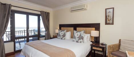 A bedroom with a large bed, a nightstand, a chair, and a view of the sea through a balcony door.