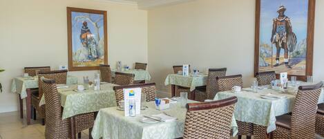 A dining area with tables set for service, wicker chairs, and framed artwork on the walls.