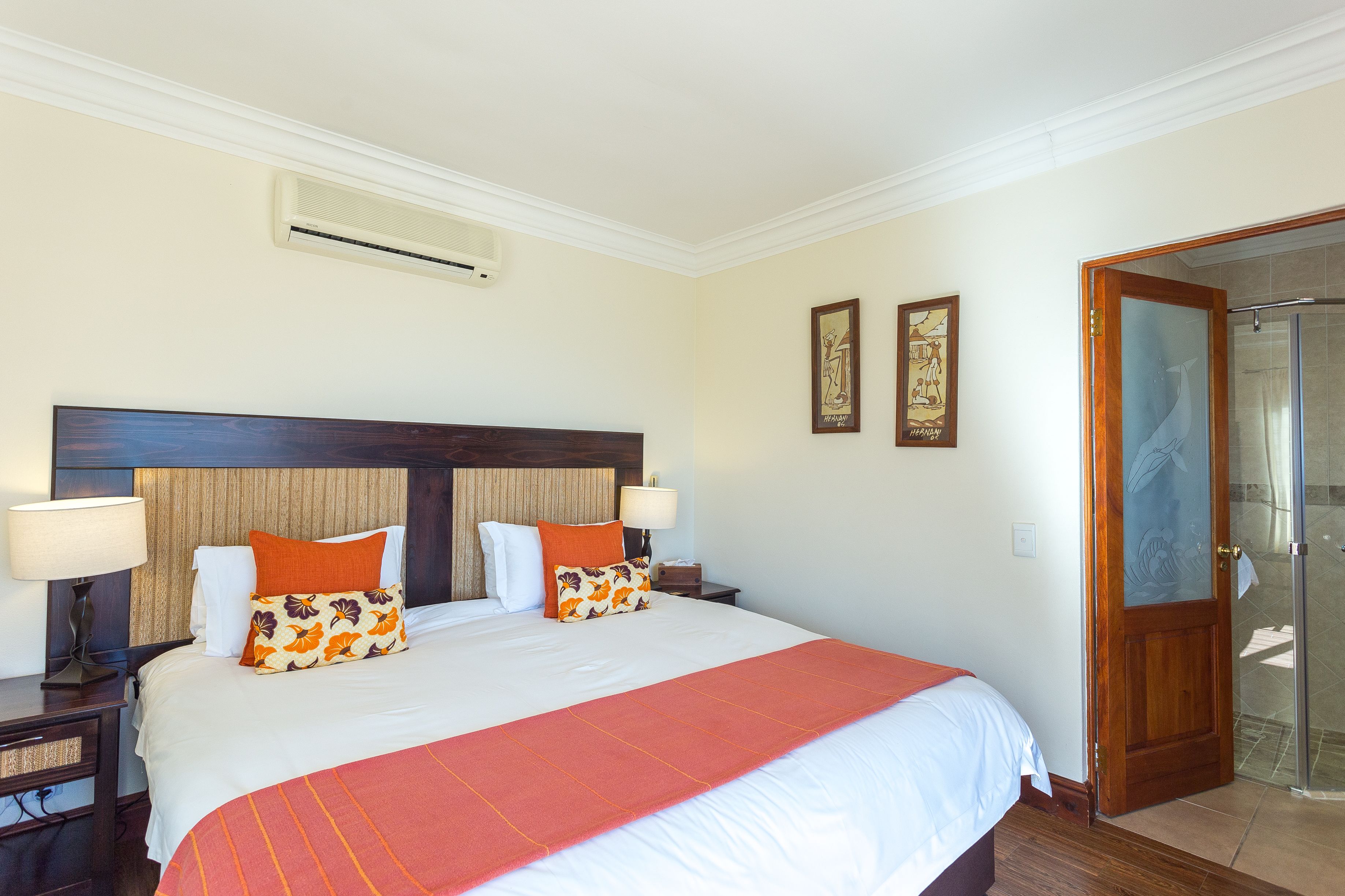 Une chambre d’hôtel avec un grand lit, deux tables de chevet, une tête de lit en bois, un plaid rouge et une porte de douche en verre.