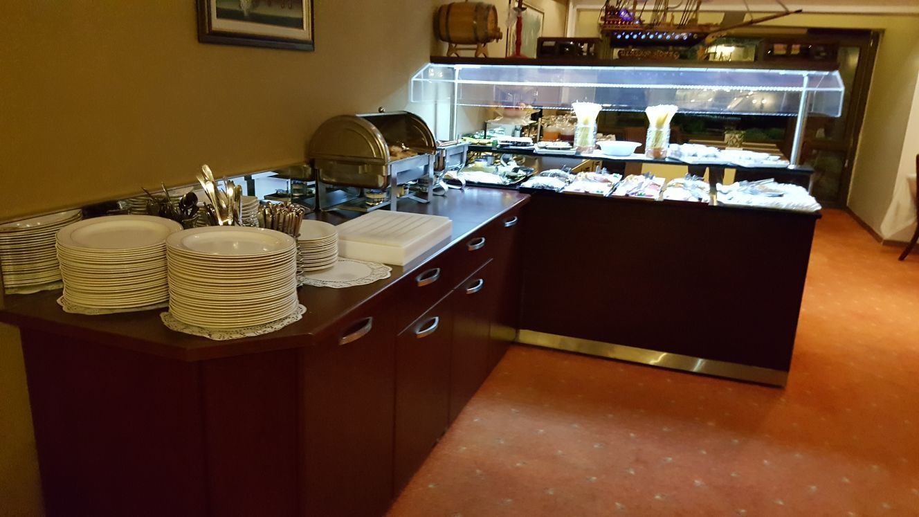 A buffet setup with stacked plates, a food display case, and a counter with utensils.