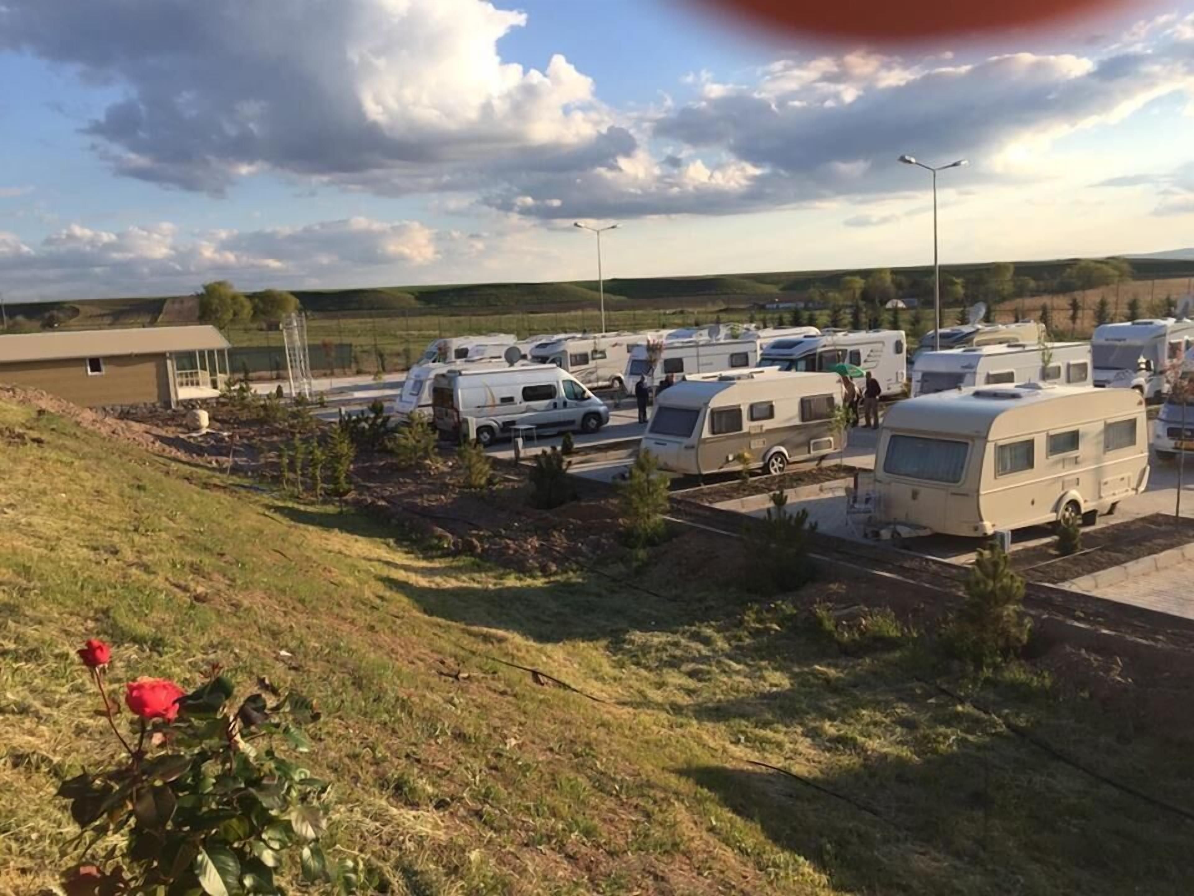 A caravan park with multiple caravans parked in designated areas, surrounded by grassy terrain and a few trees.