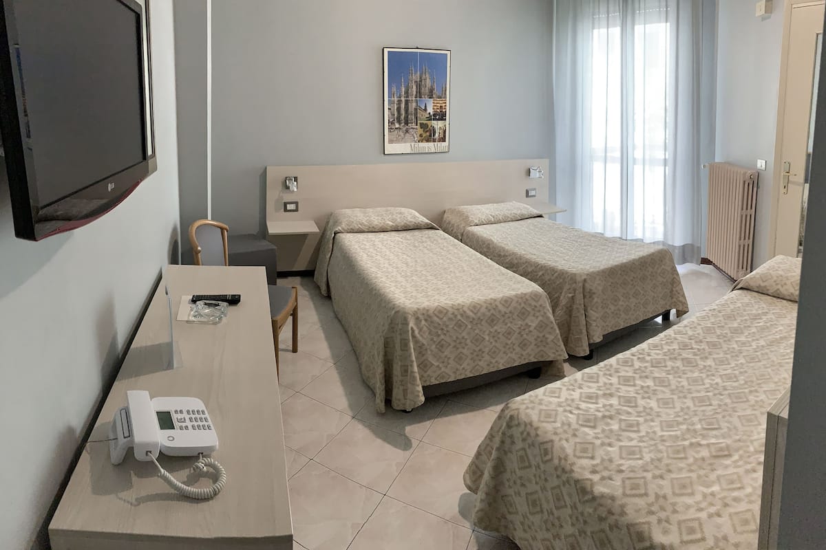 A hotel room with two beds, a desk with a telephone, a chair, a poster on the wall, and a radiator.