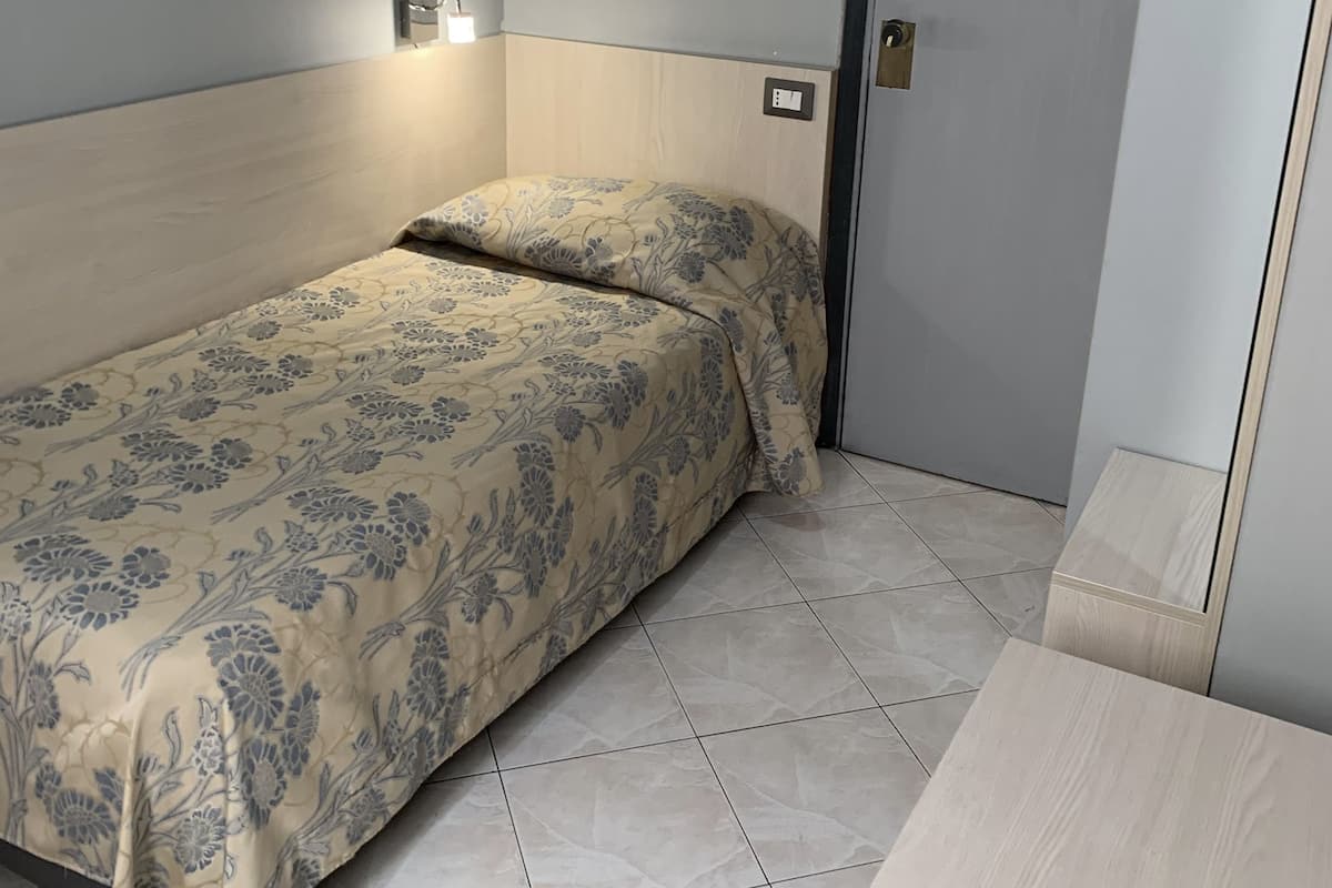 A small, neatly made bed with floral bedding in a room with light-colored walls and a tiled floor.