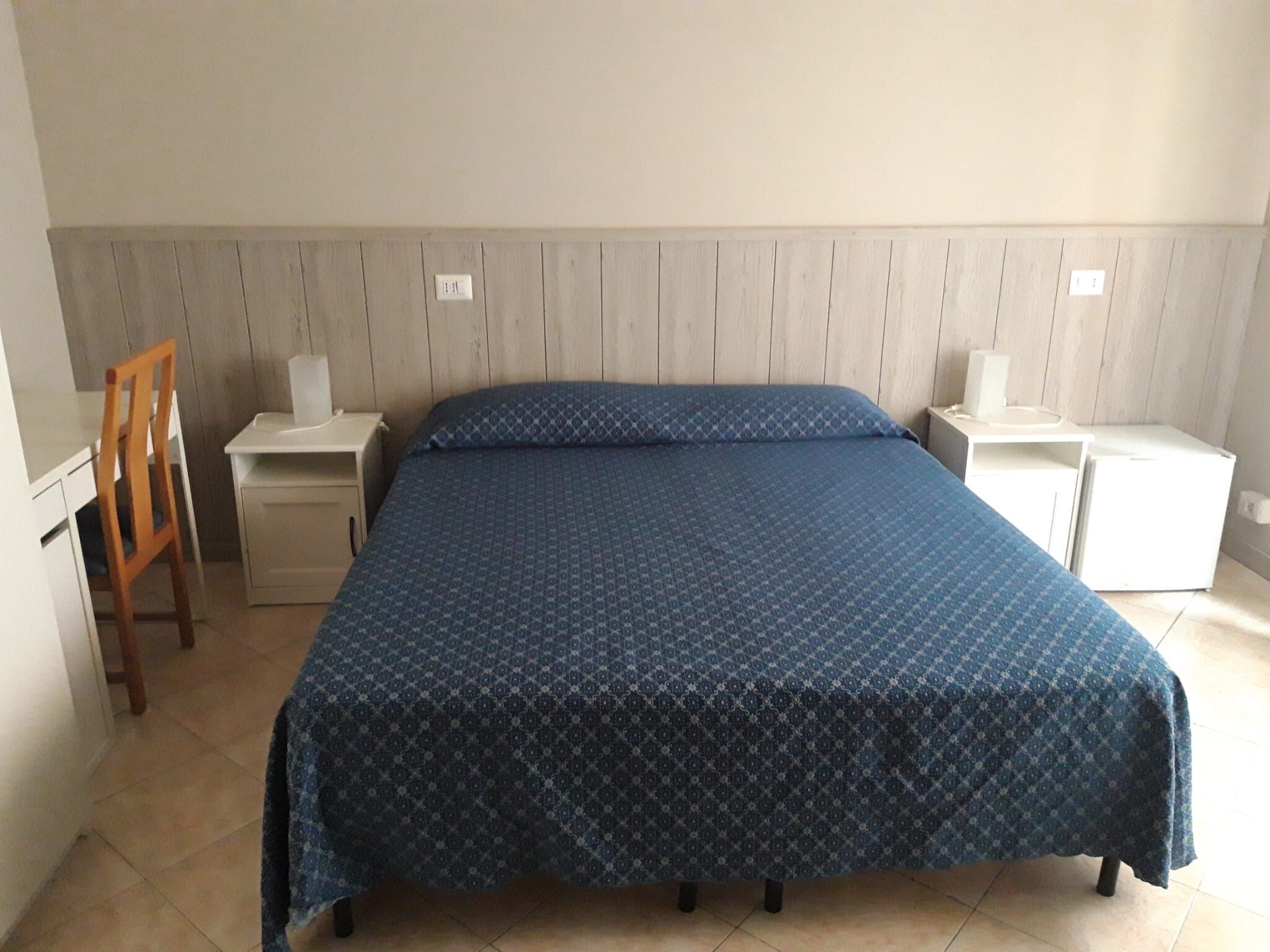 A bedroom with a bed, two bedside tables, a chair, and a wardrobe.
