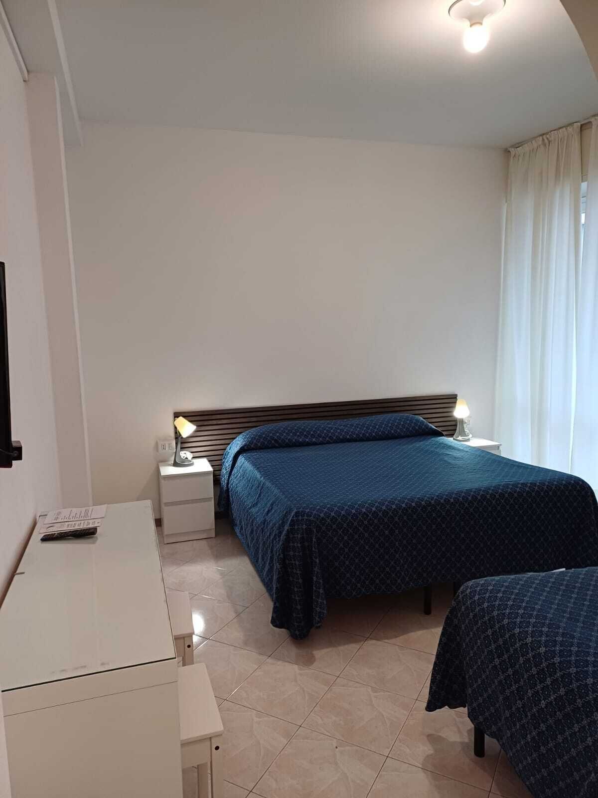 A bedroom with a bed, bedside table, lamp, and a desk with a chair.