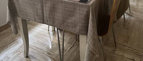 Comedor con una mesa lista para dos personas, con mantel estampado y un cuenco de cubiertos.