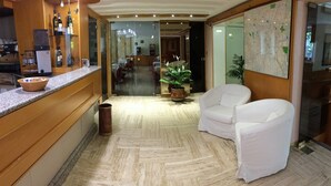 A hotel lobby with a reception desk, a coffee machine, a potted plant, and two white armchairs. - Hotel Città Studi (Milan)