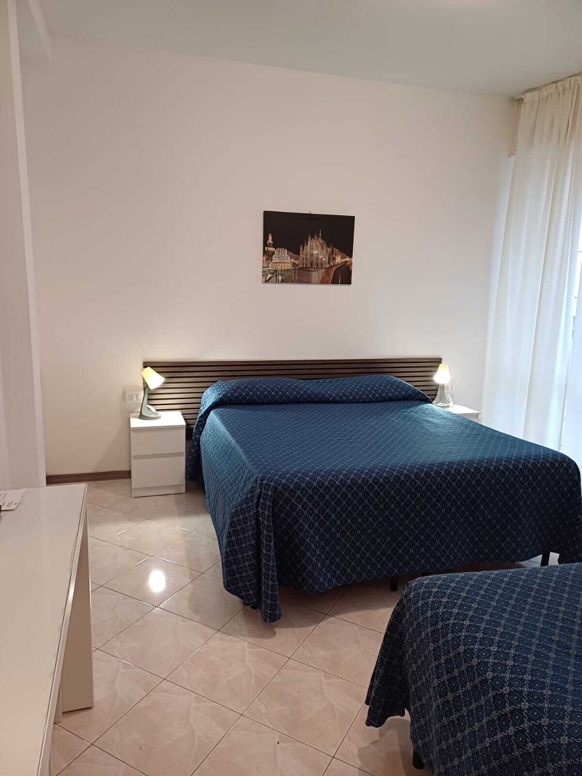Une chambre d’hôtel avec un lit, une table de chevet, un bureau et un tableau représentant une vue de la ville accroché au mur.