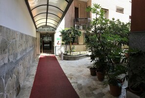 A hotel entrance with a red carpet, stone walls, and potted plants. - Hotel Città Studi (Milan)