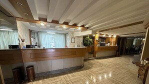 A hotel reception area with a wooden reception desk, a trash bin, and a herringbone-patterned floor. - Hotel Città Studi (Milan)