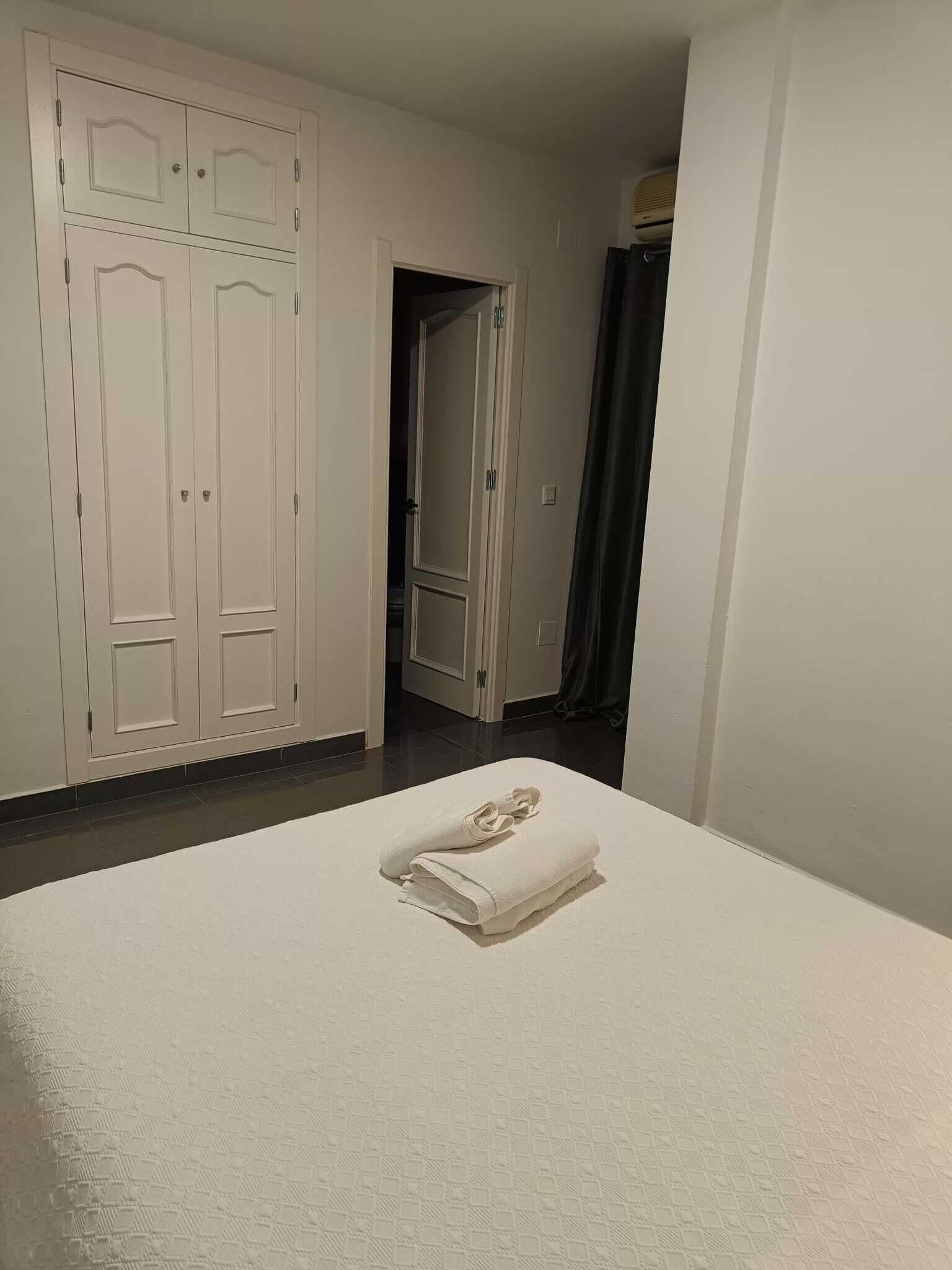 A hotel room with a bed, a wardrobe, and a bathroom visible through an open door.