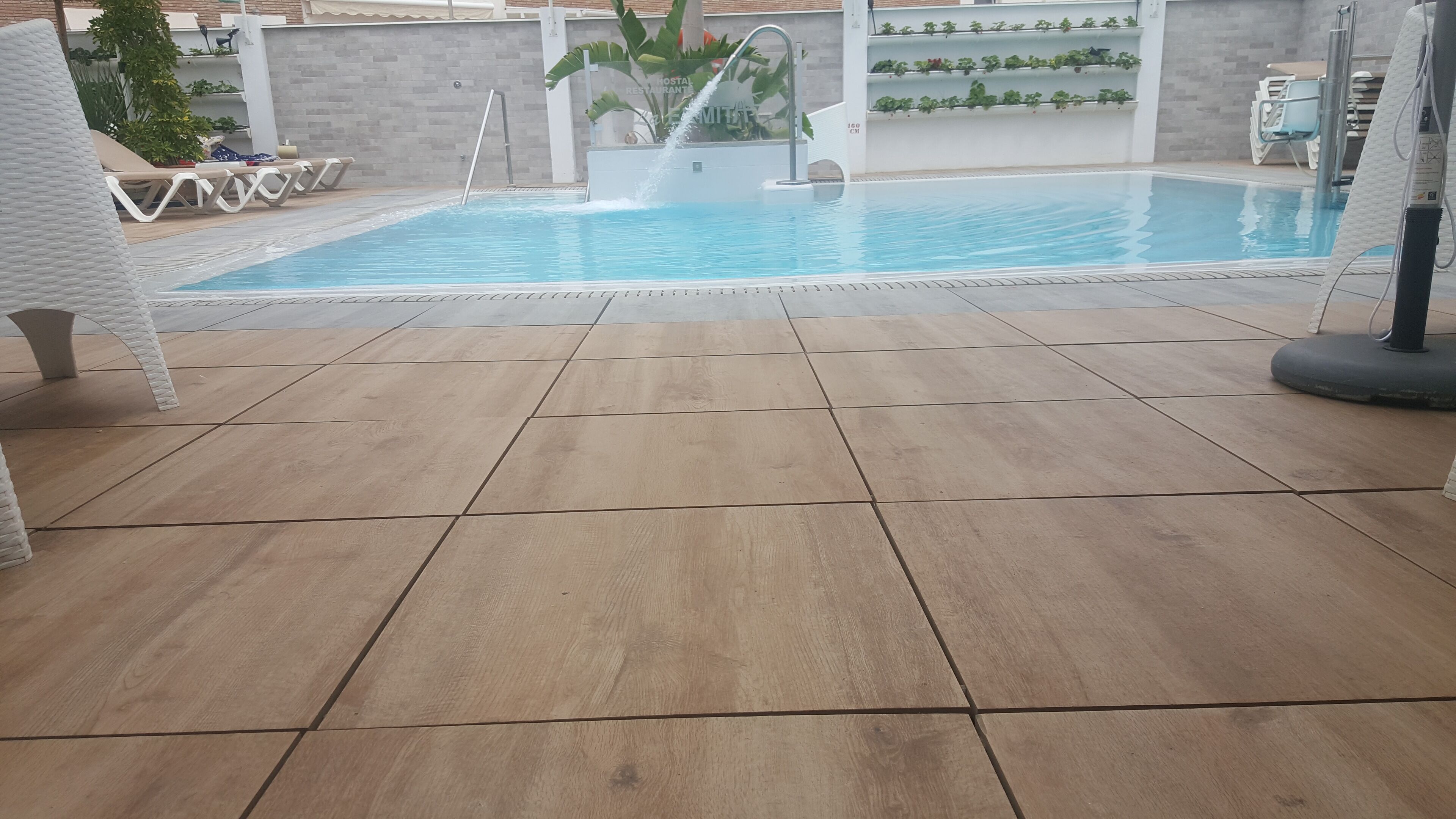 Una piscina con bordo piastrellato, poltrona relax e elemento decorativo a tema acqua.
