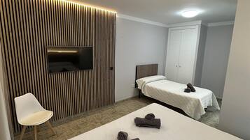Hotelkamer met een groot bed, een televisie bevestigd aan een lambrisering, een witte stoel en een tweede bed met een witte spreidek.