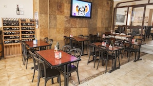 A restaurant with multiple tables and chairs, a wine rack, and a television mounted on the wall. - Hostal La Ermita (Nerja)