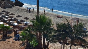 A beach with palm trees, umbrellas, and a clear view of the sea. - Hostal La Ermita (Nerja)