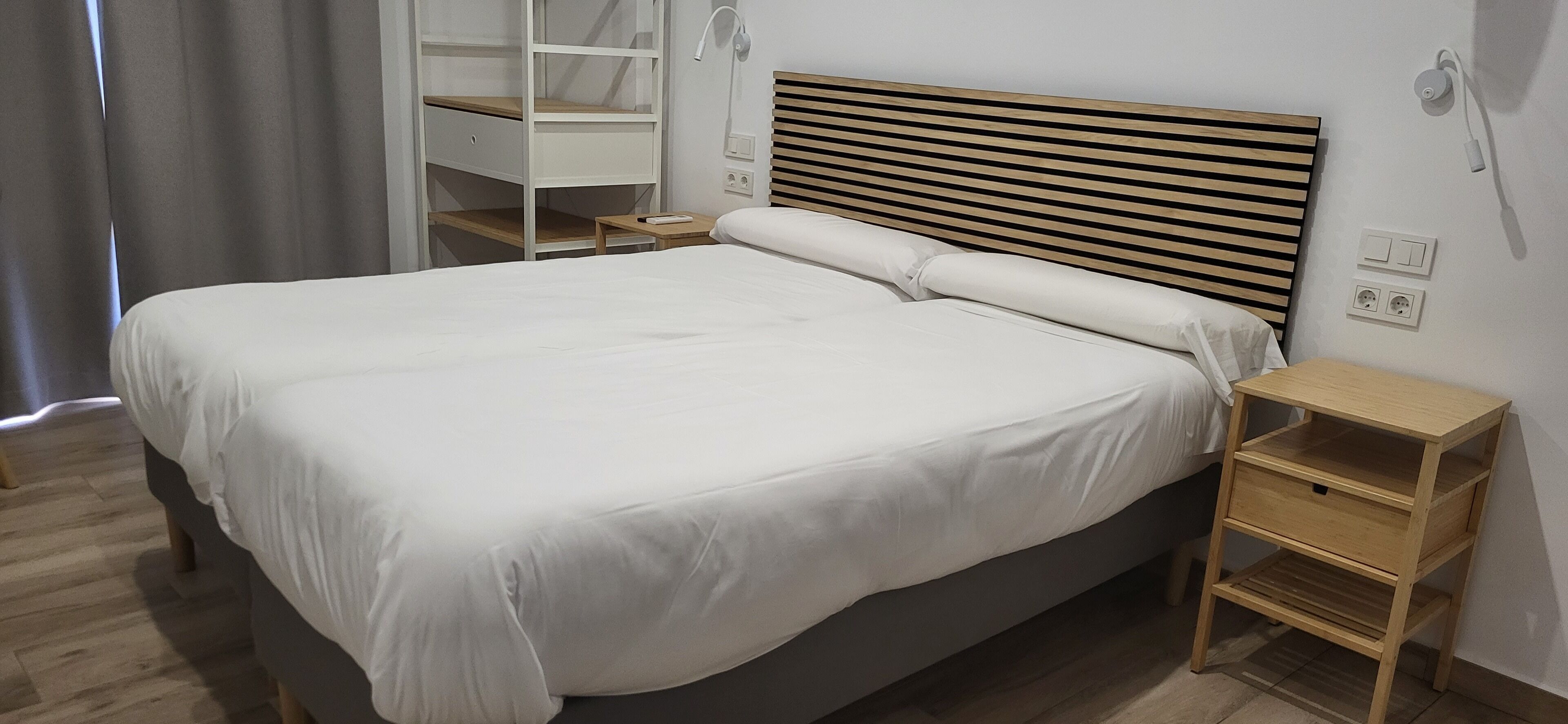 A neatly made bed with a wooden headboard, a bedside table, and a built-in wardrobe with a mirror.