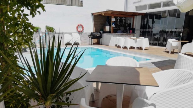 A poolside area with white wicker chairs, a glass table, and a bar area with a view of the pool. - Hostal La Ermita (Nerja)