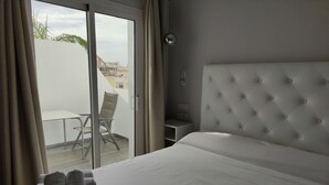 A hotel room with a bed, a chair, a table, and a view of buildings outside. - Hostal La Ermita (Nerja)