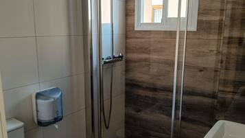 A modern bathroom with a glass-enclosed shower, a toilet, a hand dryer, and a sink.