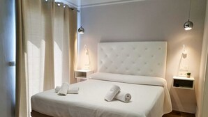 A neatly made bed with two rolled towels, a bedside table with a lamp, and a small shelf with a plant and a phone. - Hostal La Ermita (Nerja)