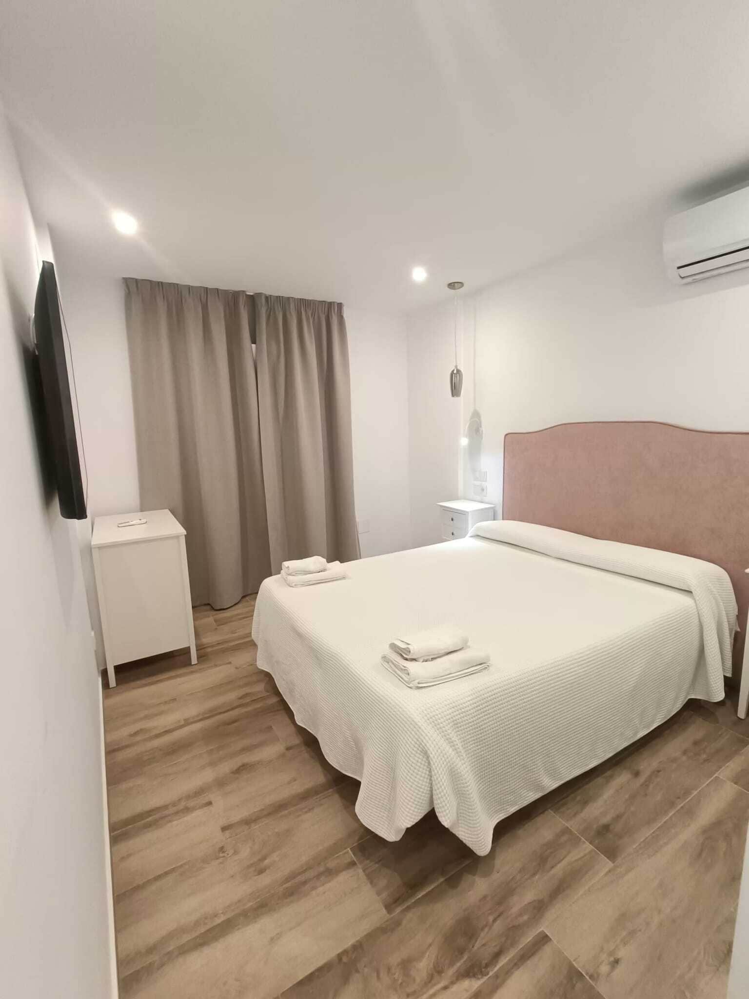 A modern bedroom with a large bed, a bedside table, a nightstand, a flat-screen TV, and a window with curtains.