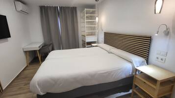 A modern hotel room with a large bed, a bedside table, a TV mounted on the wall, and a built-in shelving unit.