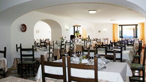A restaurant with multiple tables and chairs, white walls, and a view of the sea. - Hotel al Bosco (Forio)