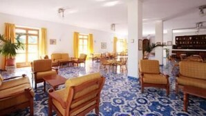 A hotel lobby with a blue patterned floor, yellow curtains, wooden furniture, and a bar area. - Hotel al Bosco (Forio)