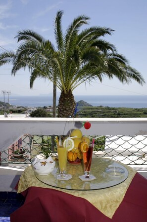 Une table avec des boissons et un saladier de fruits, donnant sur un palmier et offrant une vue panoramique sur la mer.